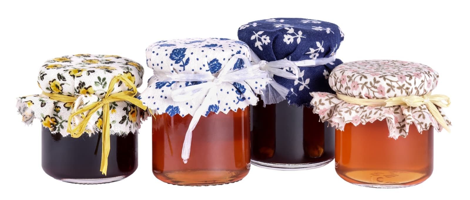Four jars of homemade jam and honey topped with floral fabric covers tied with raffia.